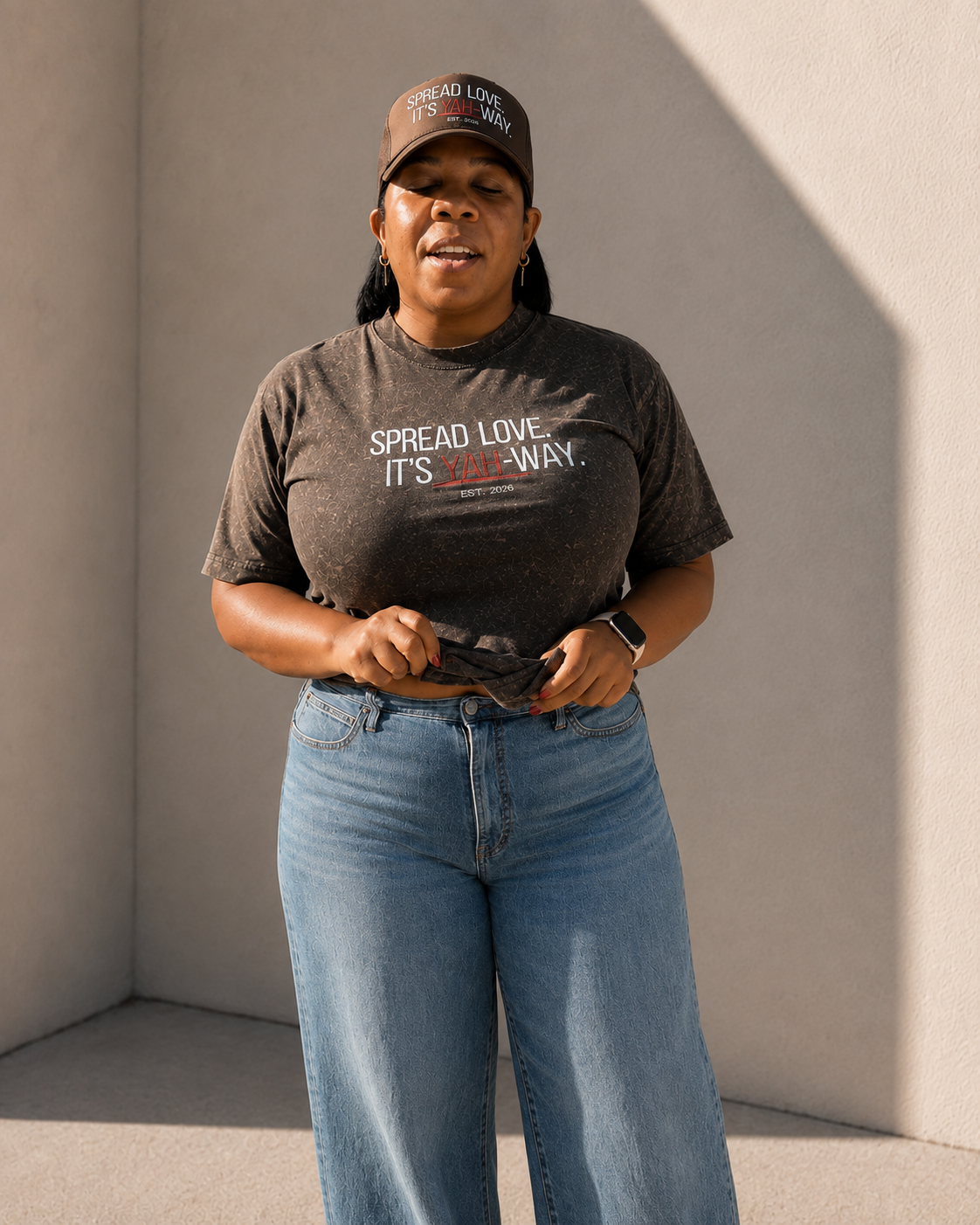 A woman wearing a God & Grit acid-wash graphic t-shirt and matching cap, featuring inspirational text in a relaxed fit.