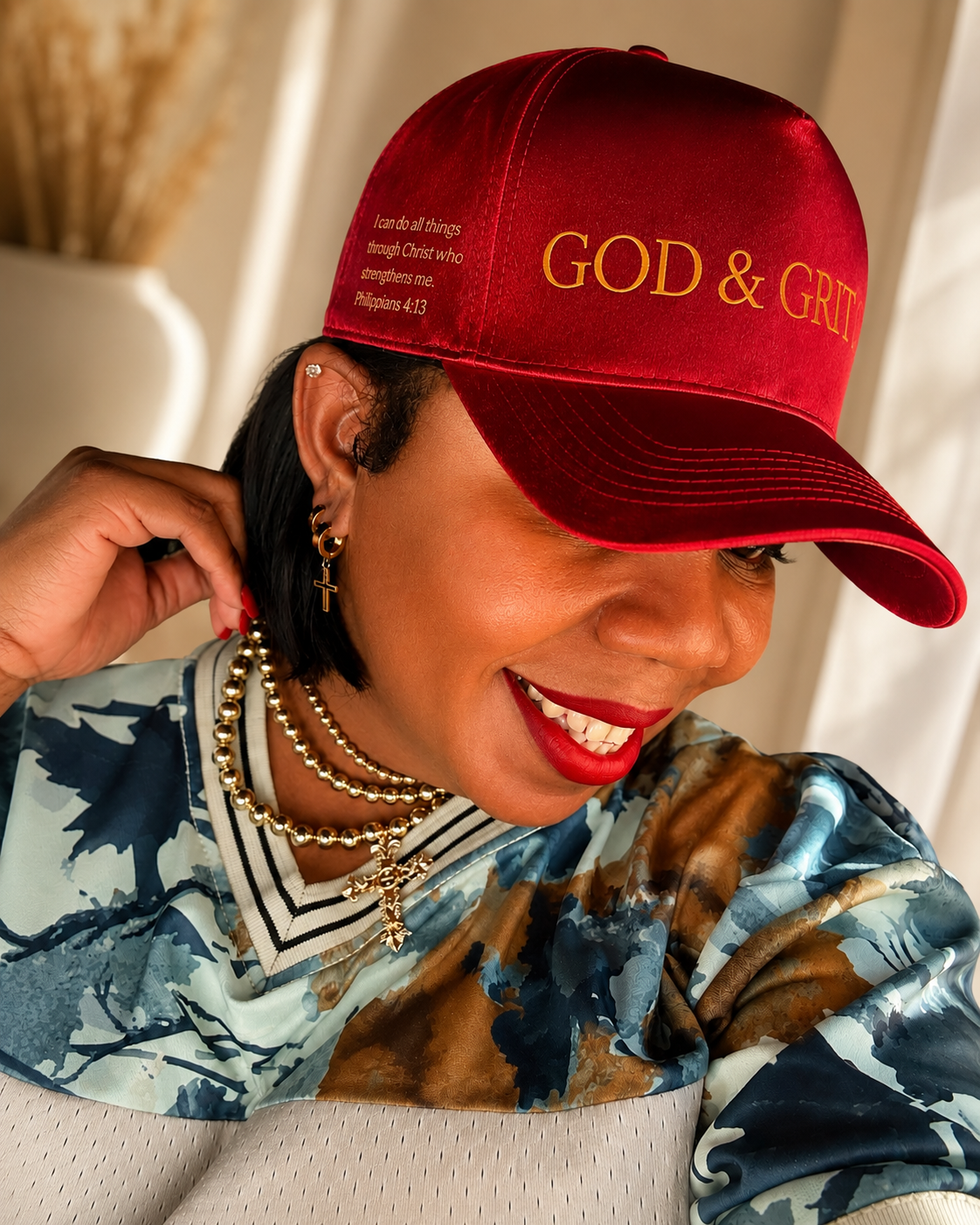 God & Grit red satin baseball cap with gold scripture embroidery worn by a woman with gold cross jewelry